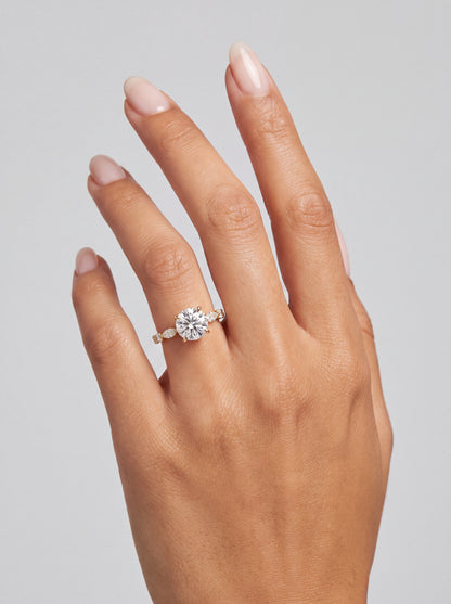 Emmeline – Runder Solitär Verlobungsring mit Akzentsteinen in Gelbgold, getragen an der Hand | Élysée Diamonds