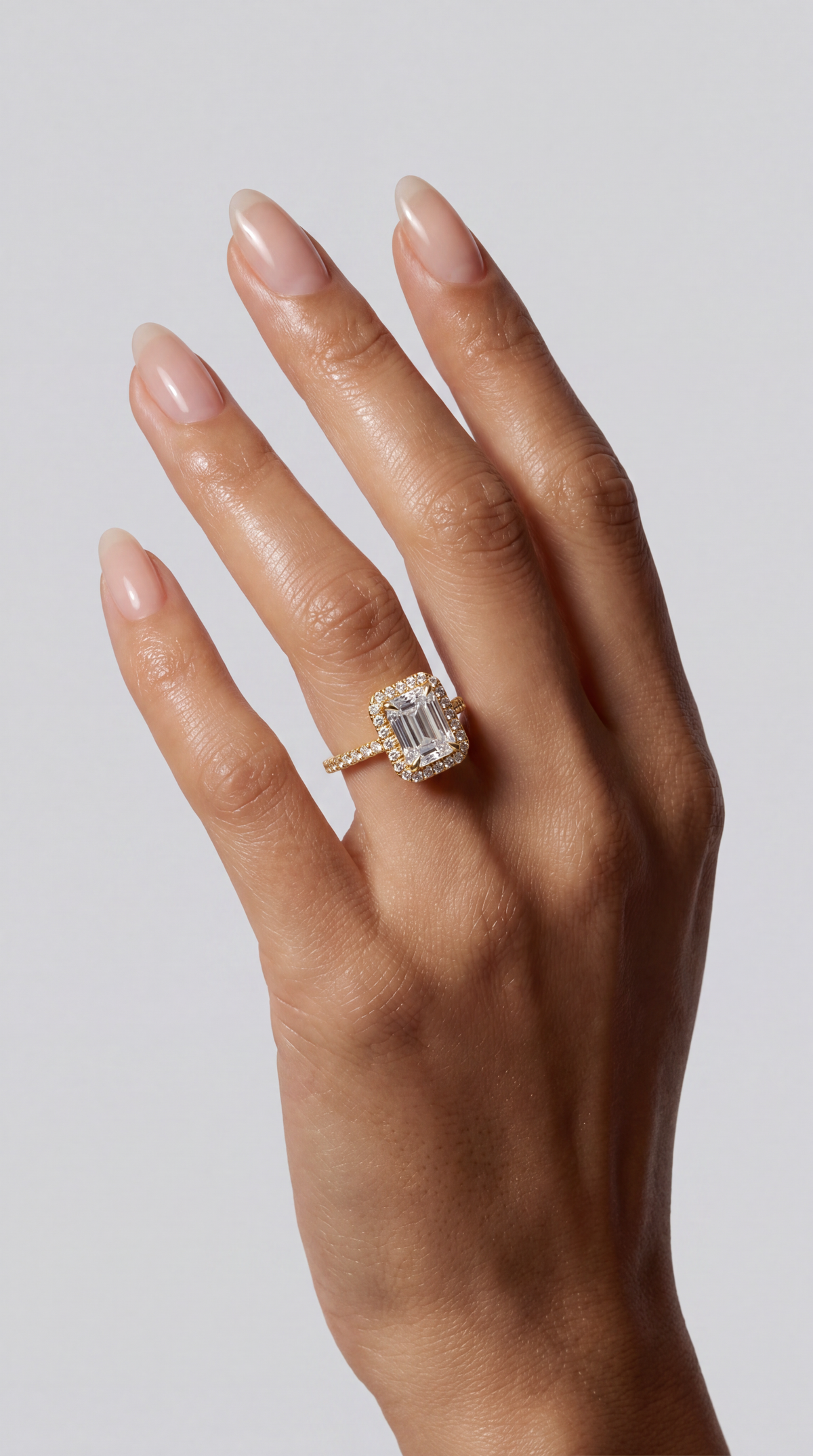 Elodie – Emerald Verlobungsring mit Halo & Pavé in Gelbgold, getragen an der Hand | Élysée Diamonds